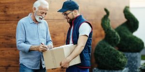 happy-senior-man-receiving-packages-signing-postman-home-delivery